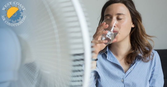 A woman sitting in front of a fan drinking a glass of water