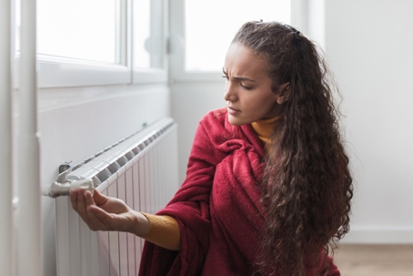 Young woman feels cold at home with sitting next to a radiator